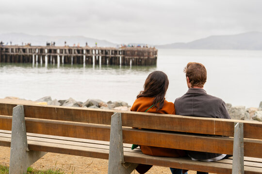 Couple Sits on Bench Watching the Water at the Pier