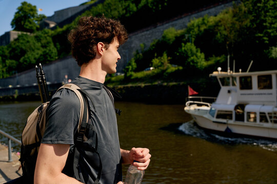 Young Man Enjoys View by the River as Boat Passes on a Sunny Day
