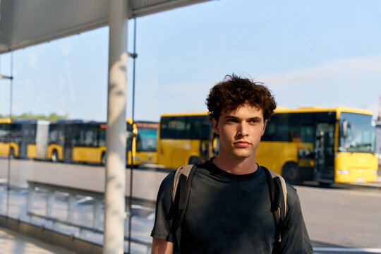 Young Man Waiting at a Bus Station With Yellow Buses in Background