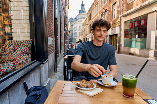 Young Man Enjoys Coffee and Dessert on a Street in a City