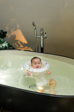 Joyful baby floats in bathtub with neck float, enjoying bath time
