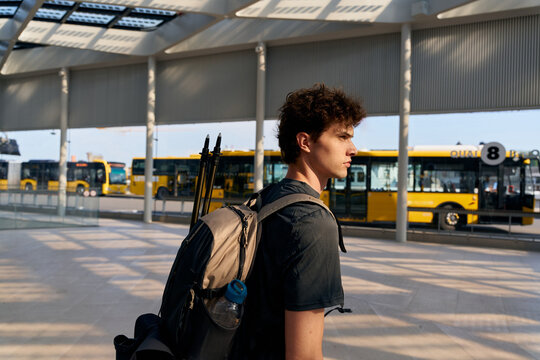 Young Man Walks Through Bus Station During Daytime With Backpack