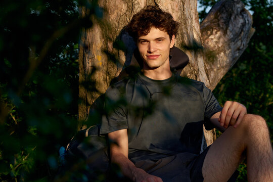 Young Man Resting Under a Tree in a Forest During Sunset