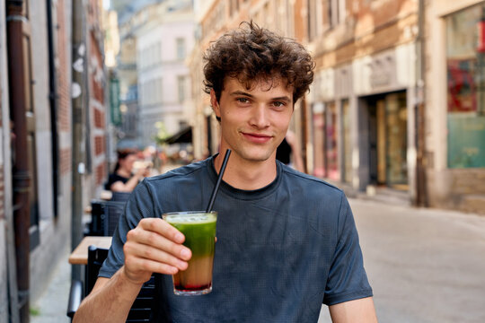 Young Man Enjoys Drink at Outdoor Cafe in City Street