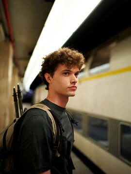 Young Man Waits at Train Station Platform With Bag and Pens