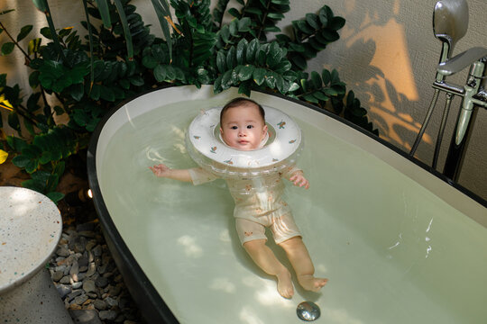 Adorable baby floats peacefully in a bathtub wearing neck float