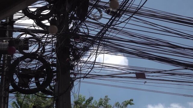 Messy power wires are tangled on the electrical pole, creating a chaotic arrangement of internet cables and powerlines in Thailand.