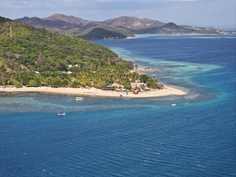Aerial view of Castaway Island featuring a sandy beach, dense tropical forest, and clear turquoise waters of the coral reef in Western Division, Fiji.