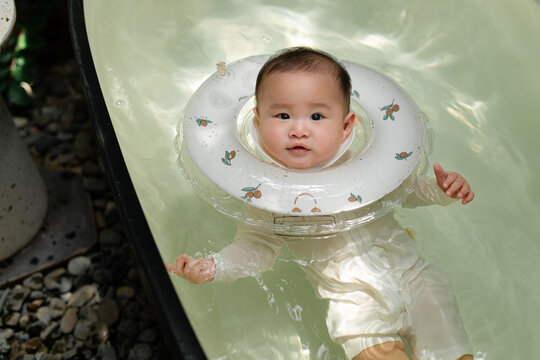 Adorable baby floats peacefully in clear water wearing neck float