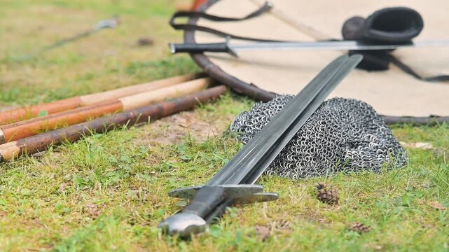 A medieval reenactment shows swords and chainmail laid on grass, surrounded by wooden tools.