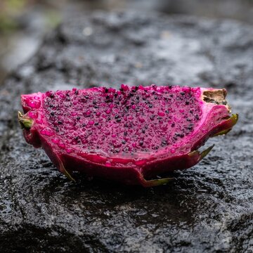 Dragon fruit rests on a wet dark stone surface displaying its bright magenta flesh and small seeds.