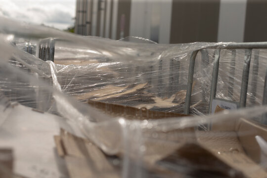 Plastic wrapped pallets near loading area, cling film shimmering over stacks of flattened cartons inside metal trolleys, scene suggests surge in ecommerce