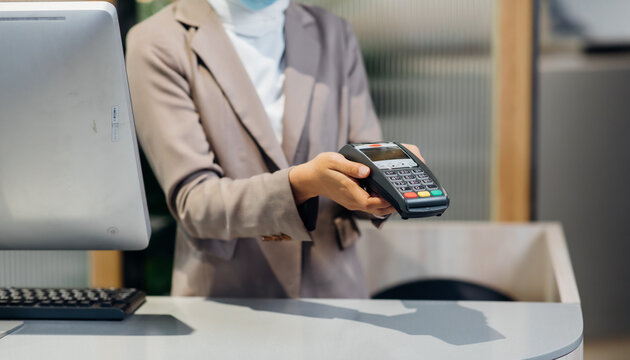 Female receptionist employee holding card reader machine on hand at checkout counter.
