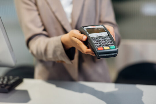 Female receptionist employee holding card reader machine on hand at checkout counter.