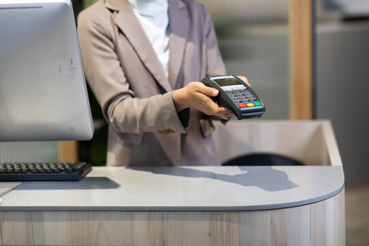Female receptionist employee holding card reader machine on hand at checkout counter.