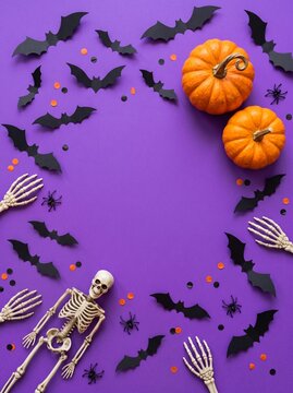 Halloween background with pumpkins skeleton and bats arranged in a circular frame on a vibrant purple surface