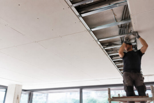 Trabajador instalando paneles en el techo de una habitaci&oacute;n en construcci&oacute;n durante el d&iacute;a