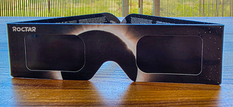 Denia, Spain &mdash; August 07, 2026. Front view of protective paper solar eclipse glasses featuring branding and safety instructions placed on a wooden table.