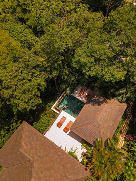 Aerial view of a luxury villa with a swimming pool nestled in a lush tropical jungle, featuring wooden sun loungers on a terrace in San Miguel, Provincia de Guanacaste, Costa Rica.