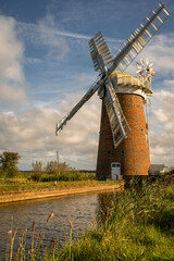 Naklejka premium Horsey Windpump beside Norfolk Broads waterway beneath a dramatic autumn sky