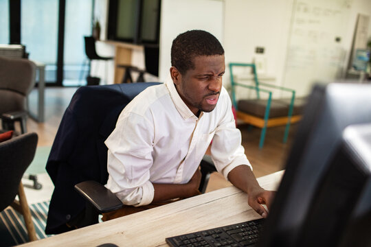 Man holding stomach while working at computer in modern office
