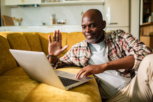 Smiling mature man waving during video call on couch at home