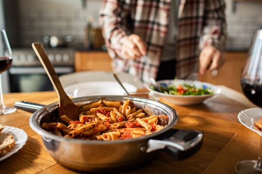 Home cook serving penne pasta at kitchen table