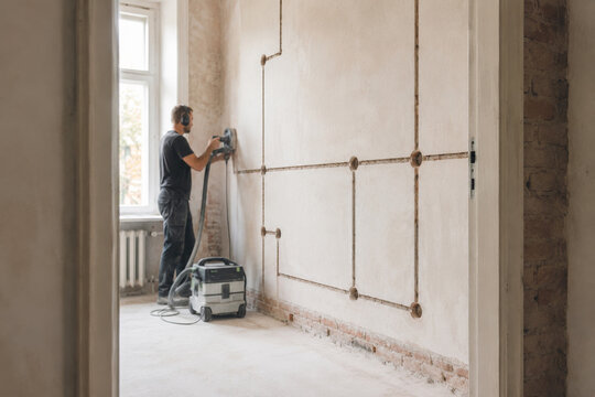 Trabajo de renovaci&oacute;n en una habitaci&oacute;n vac&iacute;a con un trabajador usando una herramienta el&eacute;ctrica en la pared