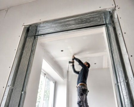 Un trabajador instala un marco de metal en una construcci&oacute;n en proceso en una habitaci&oacute;n con paredes sin acabar