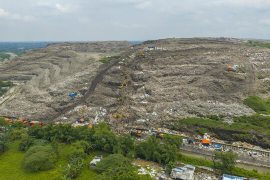 Aerial view of the Bantar Gebang landfill with heavy machinery and excavators working on massive piles of waste near lush greenery in Jakarta, Indonesia.
