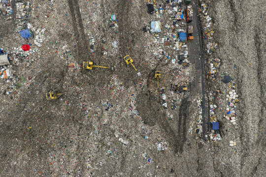 Aerial view of TPST Bantar Gebang landfill with yellow excavators moving waste piles and visible tire tracks in Kecamatan Bantar Gebang, Jawa Barat, Indonesia.