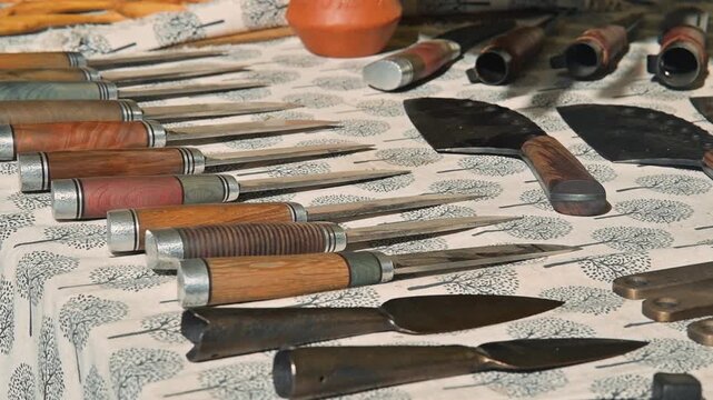 A variety of hand tools with wooden handles are laid out on a patterned cloth. These tools reflect the craftsmanship used in medieval daily life, highlighting their design and utility