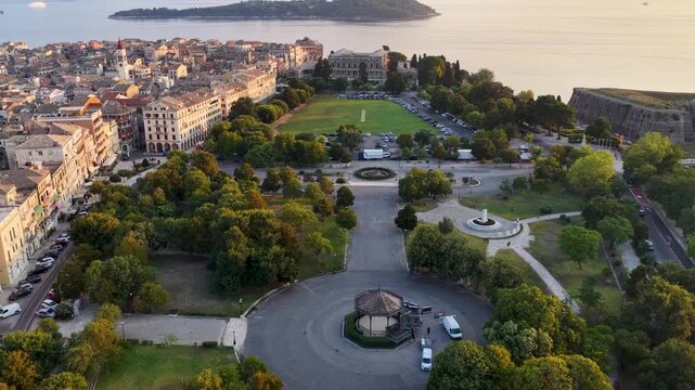 Aerial drone view of Spianada Square and the Palace of Saint Michael and Saint George in Corfu Town with lush green trees, Greece.