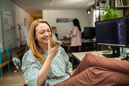 Smiling woman using voice message at desk in modern office