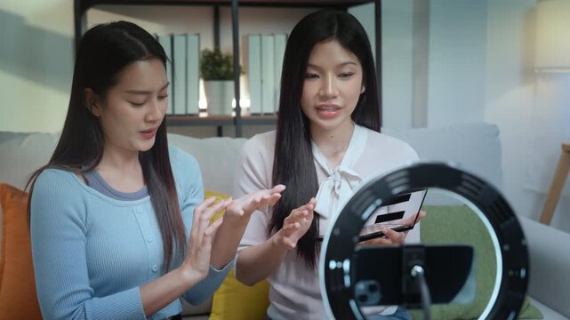 Beauty bloggers influencers live streaming makeup tutorial with ring light and smartphone in cozy living room, two friends share tips, swatching palette, friendly chat, clear demo, soft glam guide