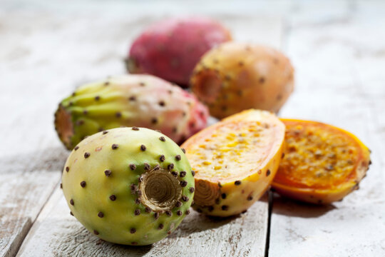 Sliced and whole prickly pears (Opuntia ficus-indica) on white wooden table, studio shot