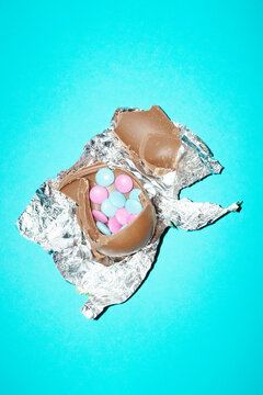 Broken chocolate Easter egg with candy inside on blue background