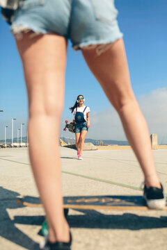 Happy young woman with longboard and headphones on beach promenade