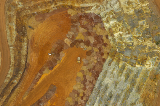 Aerial view of the gold and copper mine showing terraced excavation, heavy machinery, and colorful mineral deposits in Kecamatan Pesanggaran, Jawa Timur, Indonesia.