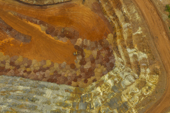 Aerial view of the Tujuh Bukit gold and copper mine featuring terraced excavation pits, heavy machinery, and exposed red earth in Kecamatan Pesanggaran, Jawa Timur, Indonesia.