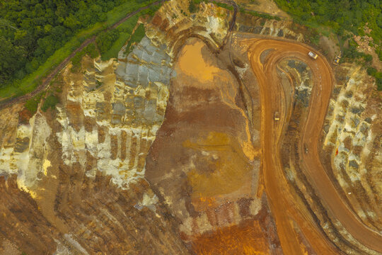 Aerial view of the open-pit gold and copper mine showing terraced excavation levels, winding haul roads, and heavy machinery in Kecamatan Pesanggaran, Jawa Timur, Indonesia.