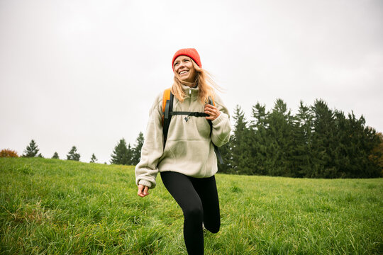 Smiling woman in beanie hikes through a green meadow for adventure