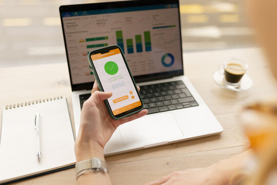 A woman analyzes financial charts on her laptop and smartphone