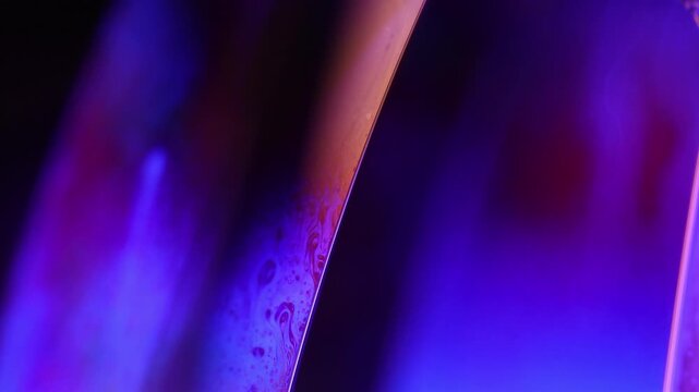 Glowing violet and amber liquid film boundary with subtle marbling. Deep violet and blue backlighting illuminates a vertical fluid plane boundary.