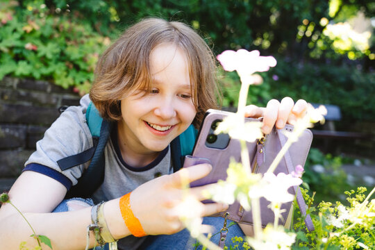 Smiling girl photographs a flower with her smartphone outdoors