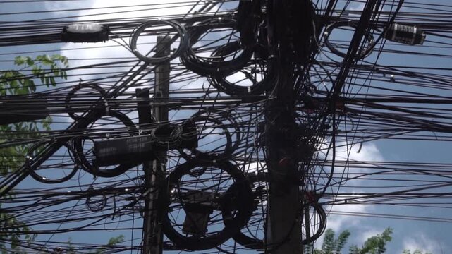 Messy power wires are tangled on the electrical pole, creating a chaotic arrangement of internet cables and powerlines in Thailand.