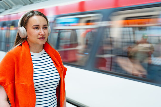 Woman waits for the subway train while listening to music