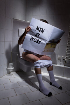 Germany, Man sitting on toilet, reading newspaper