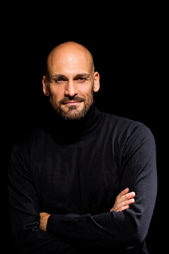 Portrait of man with crossed arms wearing black turtleneck in front of black background