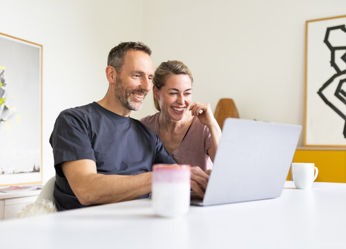Smiling couple uses a laptop together at a desk in their home office